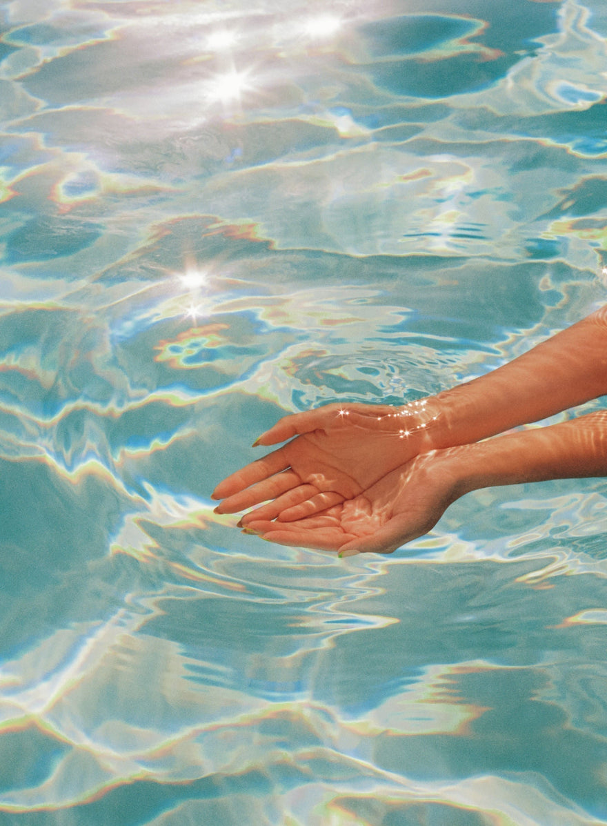 Two hands cupped in a sparkling pool of clear water with refracted rainbow light highlighting the water ripples